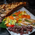 A gourmet seafood and steak platter featuring grilled langouste, merou fish fillets, and tender filet mignon, served with sautéed vegetables.